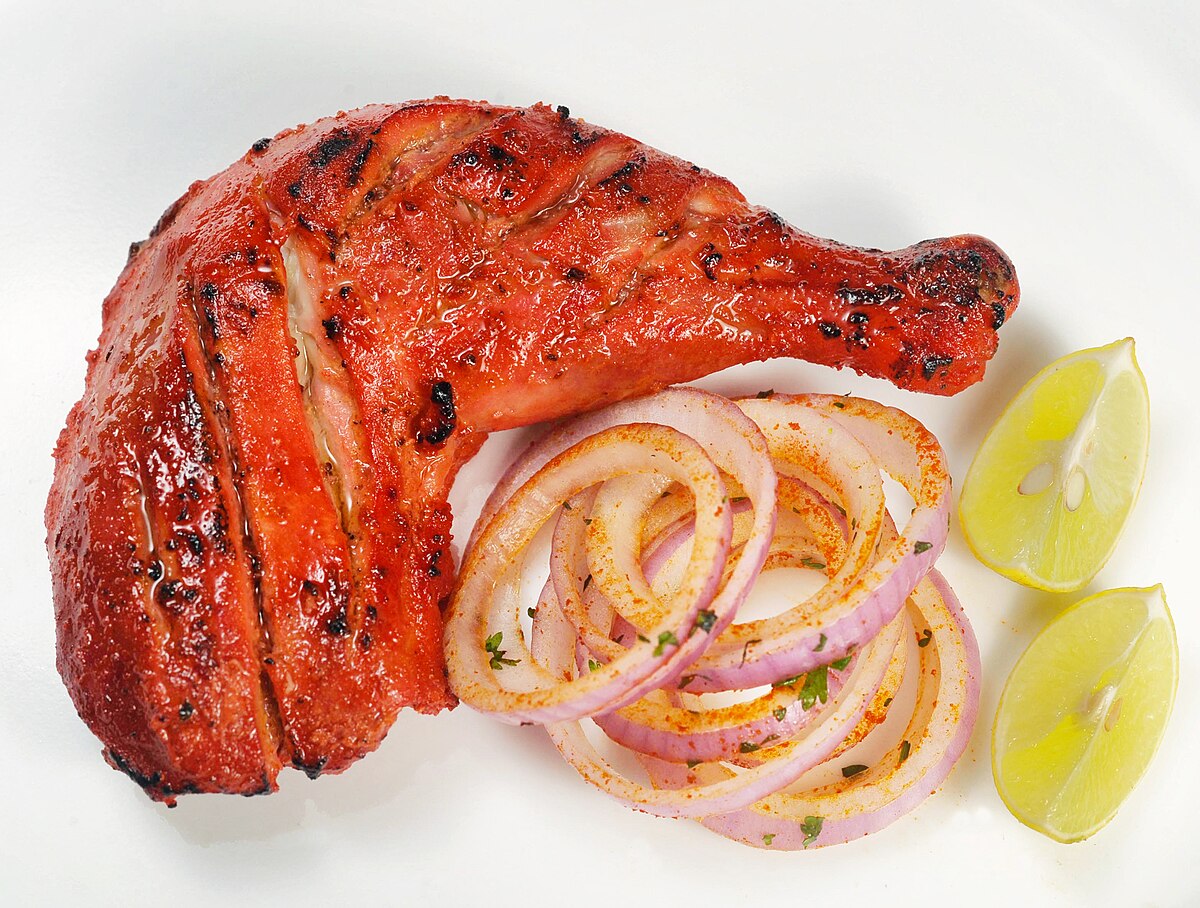 A grilled tandoori chicken leg quarter served with sliced red onions and fresh lemon wedges on a white plate at The Dine restaurant in Broxburn.